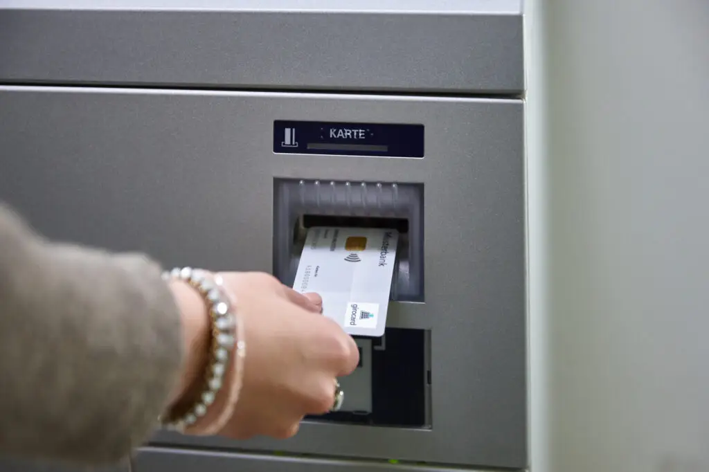 Hand, die eine Bankkarte in einen Geldautomaten einführt, mit dem Bildschirm, der die Aufforderung zur Karteneingabe anzeigt.