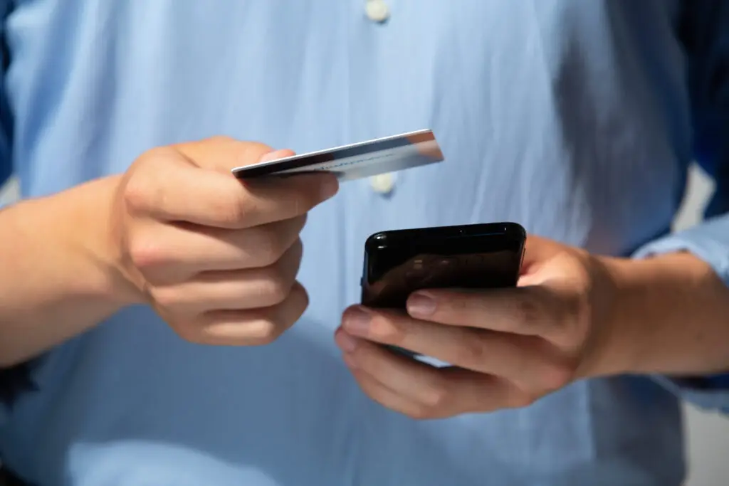 Person hält eine Kreditkarte in der einen Hand und ein Smartphone in der anderen Hand, während sie eine Online-Zahlung durchführt.