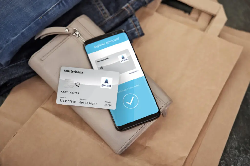 Smartphone mit digitaler Girocard-Anzeige und physischer Bankkarte auf einer Tasche und Jeans, symbolisiert moderne Zahlungsmethoden und digitale Bankdienstleistungen.