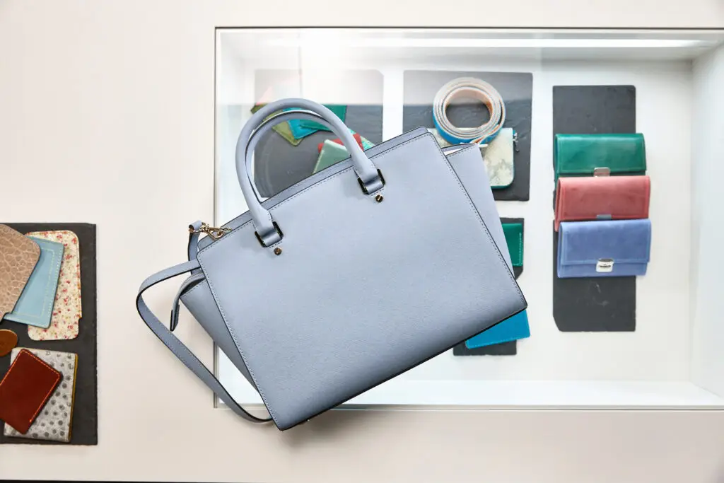 Hellblaue Handtasche aus hochwertigem Material, elegant platziert über einer Auswahl farbiger Geldbörsen in einem modernen Ausstellungsraum.