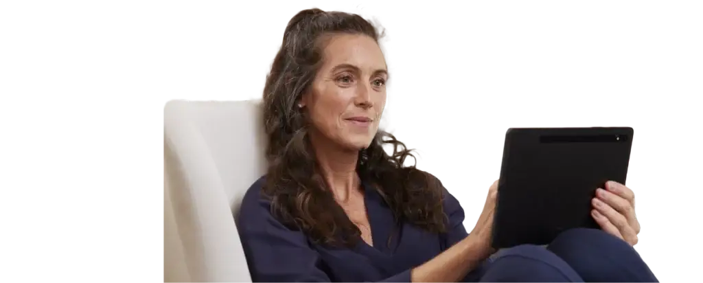 Frau mit langen, lockigen Haaren sitzt entspannt auf einem Sessel und hält ein Tablet in der Hand, während sie lächelt und den Bildschirm betrachtet.