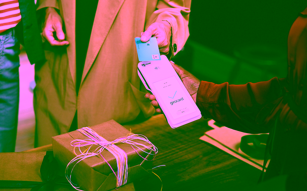 Eine Hand hält eine girocard an ein Terminal, um ein Geschenk zu bezahlen