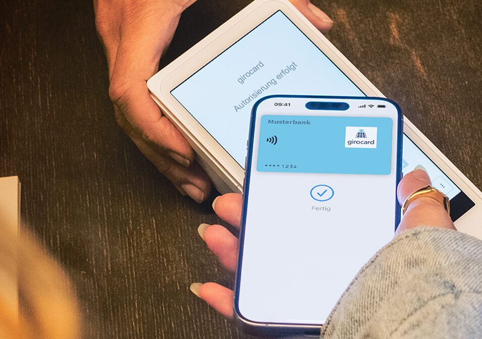 Eine blaue girocard der Musterbank wird an ein Terminal gehalten.