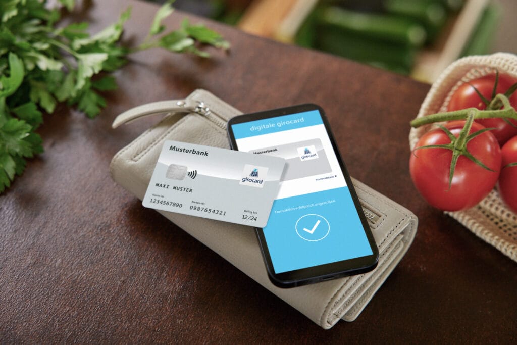 Digitale girocard und physische Bankkarte liegen auf einem Tisch neben frischen Tomaten und Kräutern, symbolisieren moderne Zahlungsmethoden und digitale Finanzverwaltung.