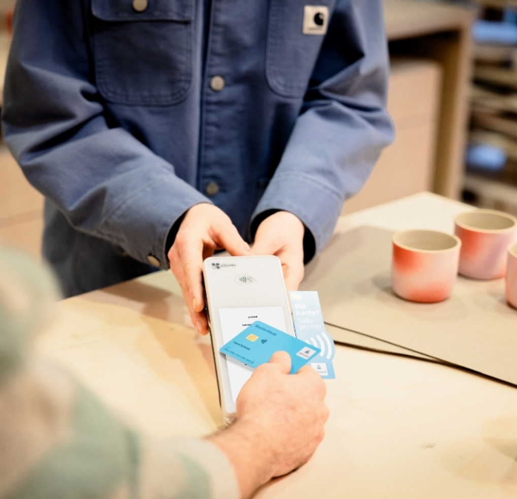 Eine Person bezahlt kontaktlos Tassen in einem Laden und hält die girocard ans Terminal.