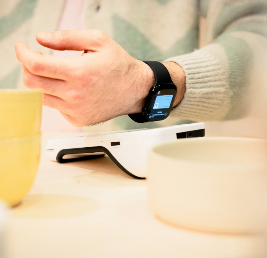 Eine Person hält ihre Smartwatch an ein Terminal, um kontaktlos zu bezahlen.