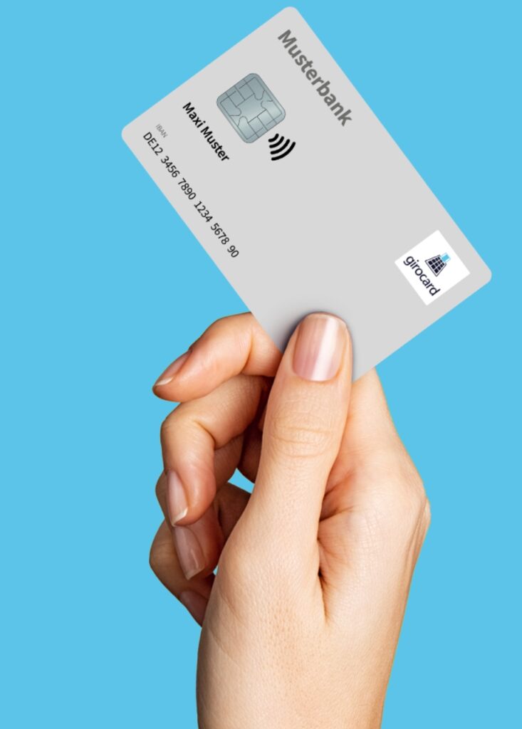 Max-Muster Girocard-Karte mit kontaktloser Zahlungsfunktion wird von einer Hand gegen einen blauen Hintergrund gehalten; auf der Karte ist der Markenname Musterbank und das girocard-Logo zu sehen.